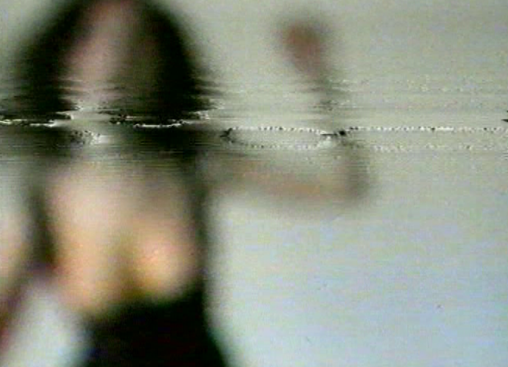 Filmstill von Pipilotti Rist aus dem Video &quot;I'm not the Girl who misses much&quot; aus dem Jahr 1986. Der Videoausschnitt zeigt die Künstlerin mit schwarzem Kleid und offenen Haaren. 